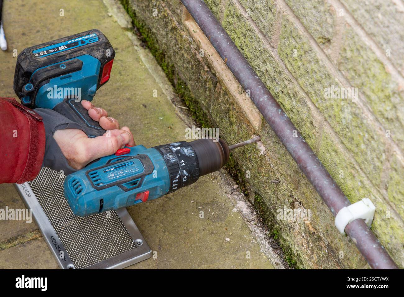 Ein Mann (Mann, Arbeiter, Handwerker), der mit einem tragbaren Bohrer Löcher in Ziegelsteine bohrt. Die Bohrungen dienen zum Anschrauben einer Abdeckung aus Luftziegeln. Stockfoto