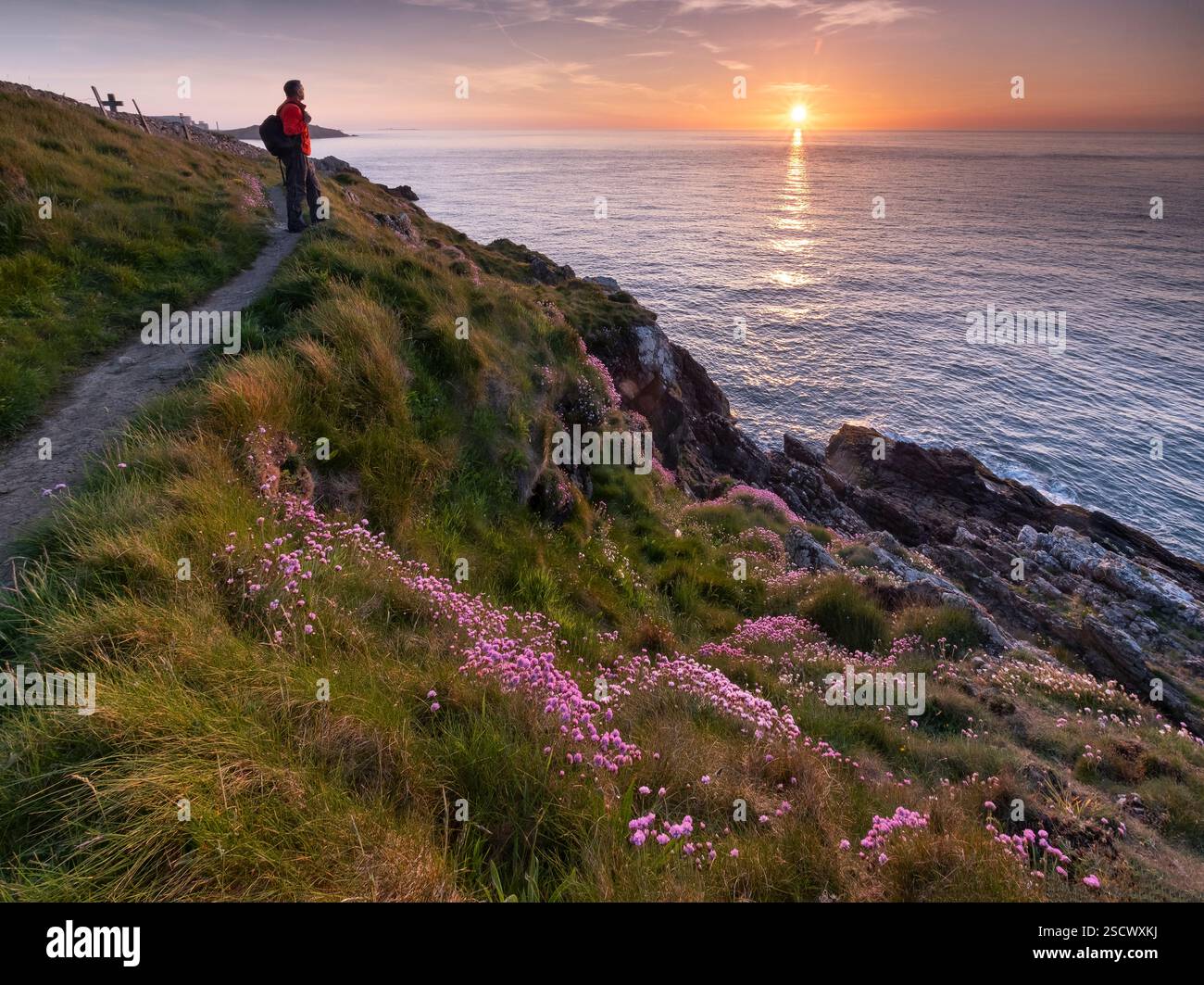 Wanderer mit Blick auf das Meer vom Anglesey Coast Path bei Sonnenuntergang im Frühjahr, in der Nähe von Cemaes, Anglesey, North Wales, Großbritannien Stockfoto