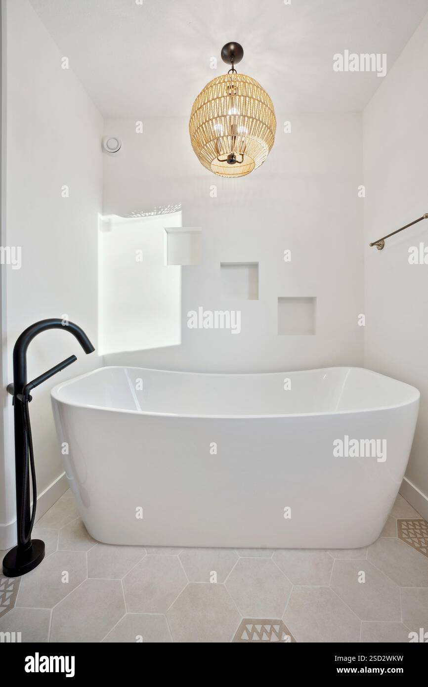 Weiße Badewanne mit schwarzem Wasserhahn und einer Hängelampe darüber. Das Badezimmer ist sauber und gut beleuchtet, was eine entspannende Atmosphäre schafft Stockfoto