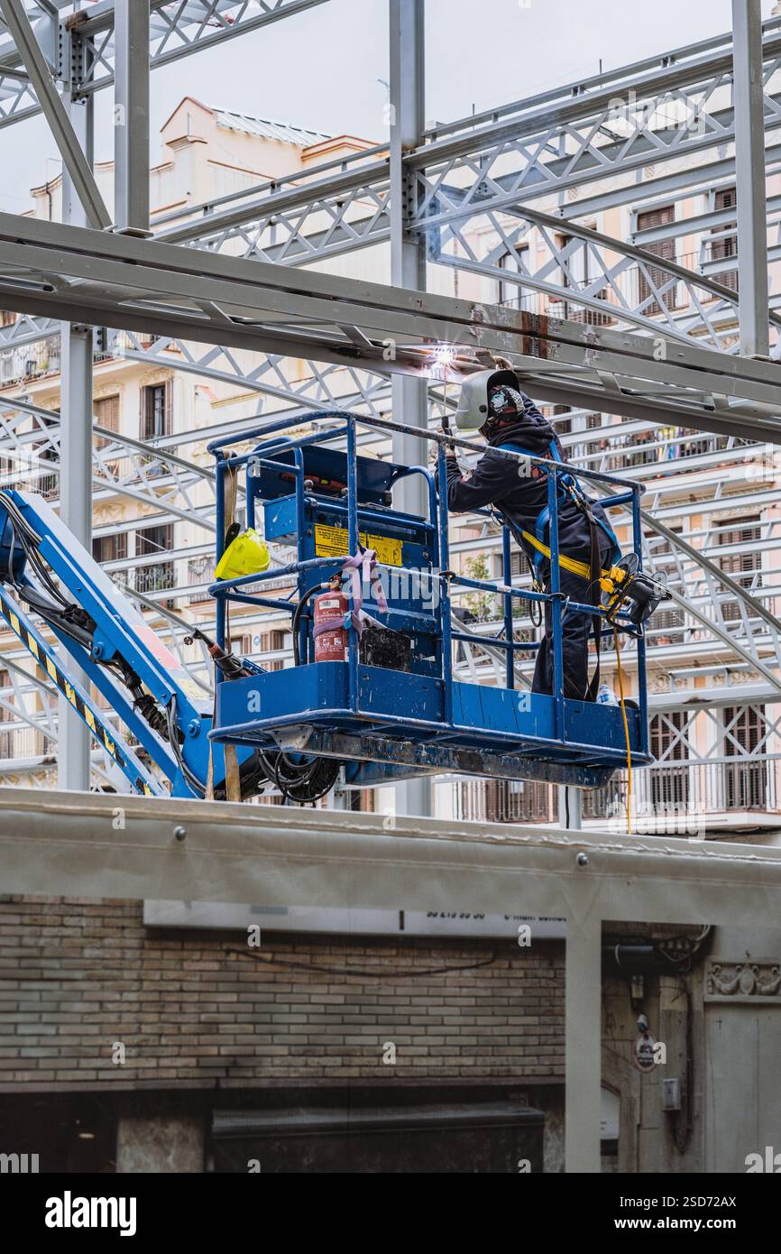 Schweißer, der Arbeitskleidung trägt, lötet eine Stahlkonstruktion, während sie auf einer Hubarbeitsbühne steht, um Sicherheit und Präzision zu demonstrieren. Stockfoto