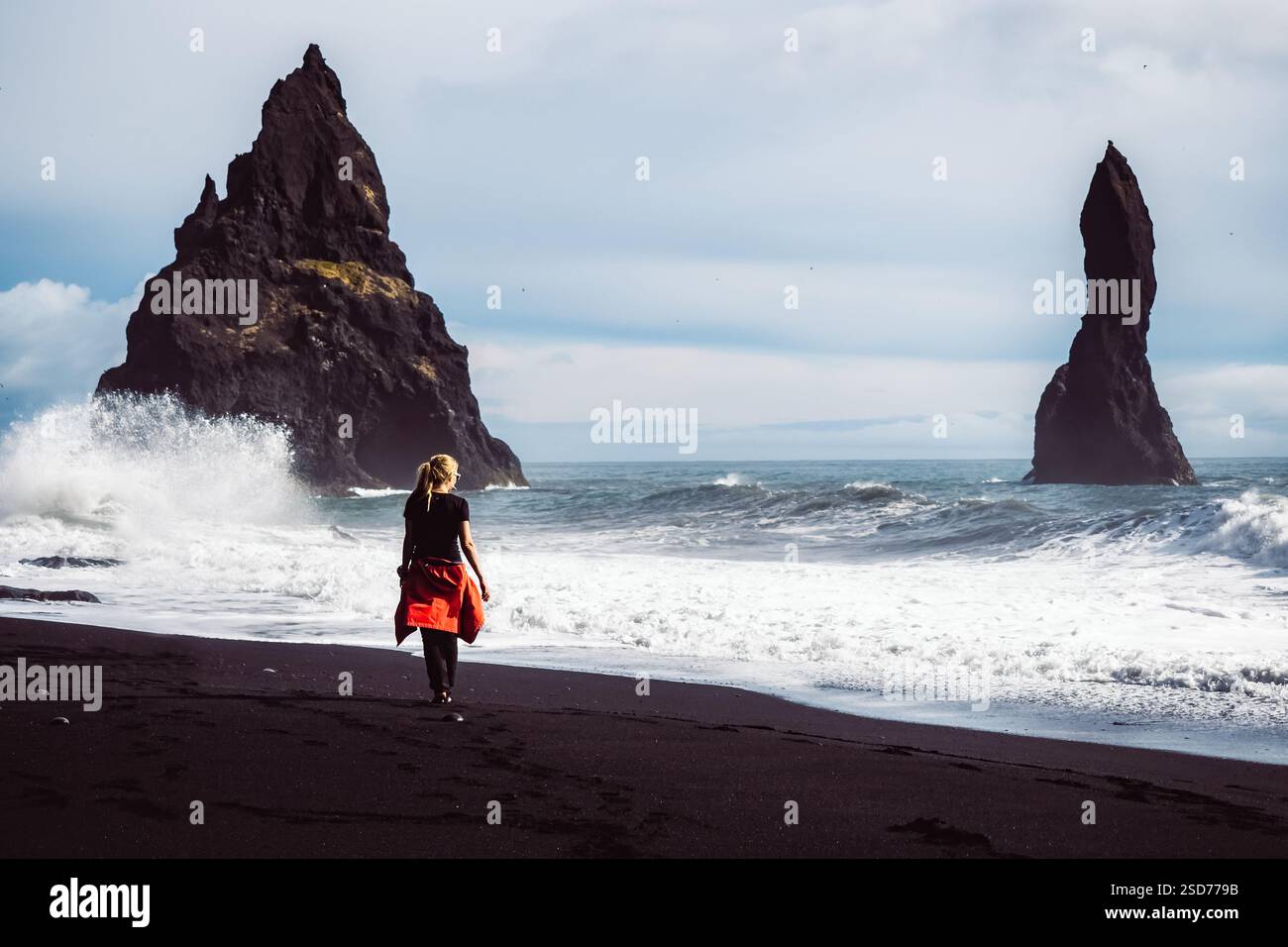 Eine Person, die entlang eines atemberaubenden schwarzen Sandstrandes Reynisfjara in Island in VIK Myrdal im Golden Circle Gebiet spaziert, mit Wellen des Atlantischen Ozeans Stockfoto