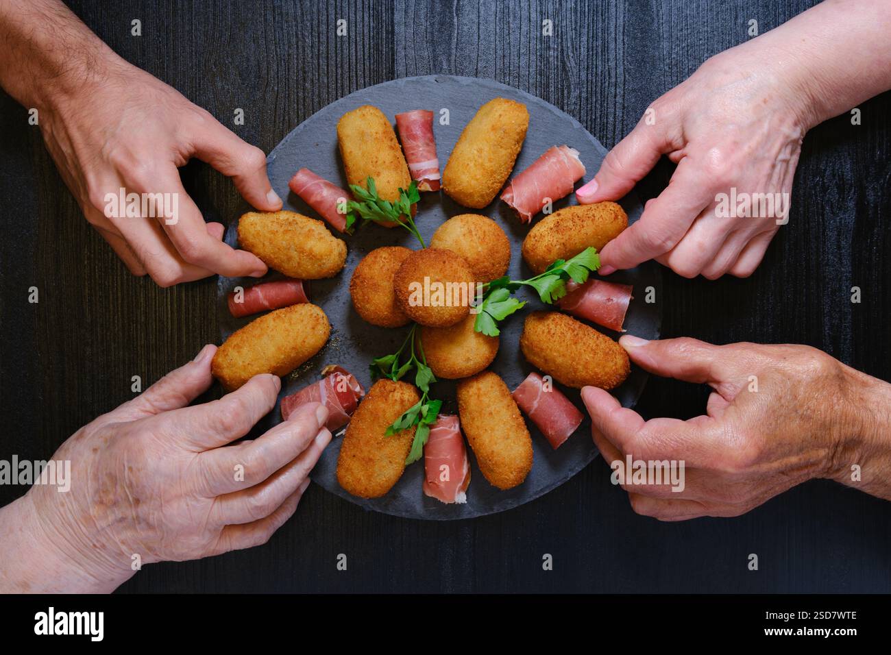 Hände nähern sich einer Schieferplatte, um Kroketten und Scheiben Serrano-Schinken aufzuheben Stockfoto