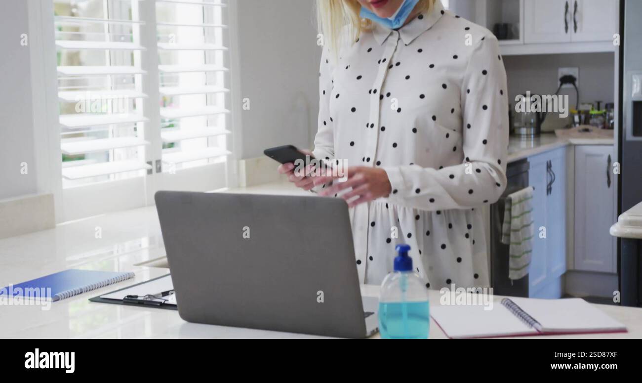 Bild einer Frau im Polka Dot Shirt mit Smartphone und Laptop in der modernen Küche Stockfoto