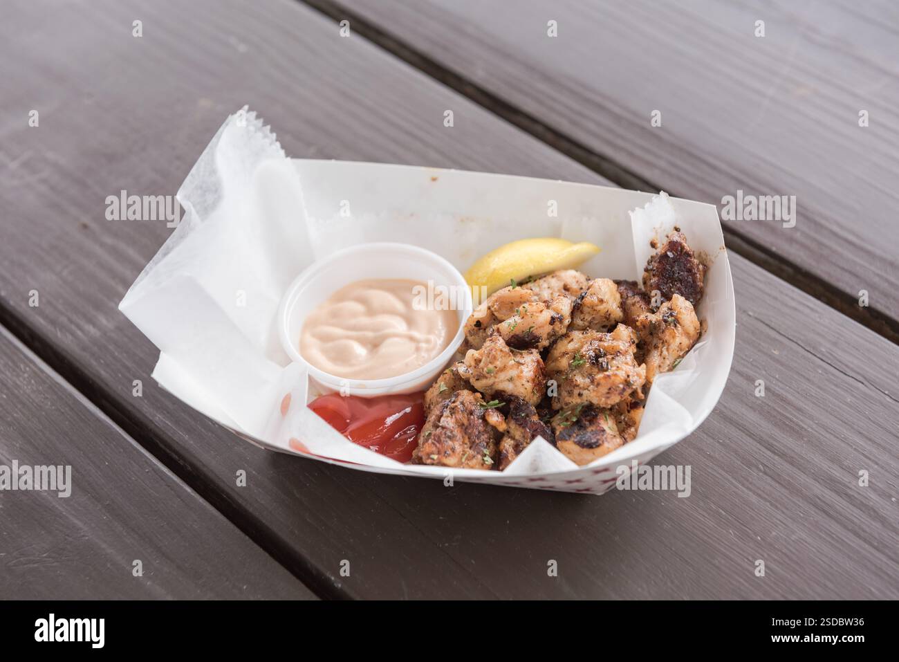 Zarte Happen von Alligator Tail gewürzt und gegrillt, serviert mit sägegrassoße, auf einem weißen Papierboot auf einem braunen Picknicktisch. Stockfoto