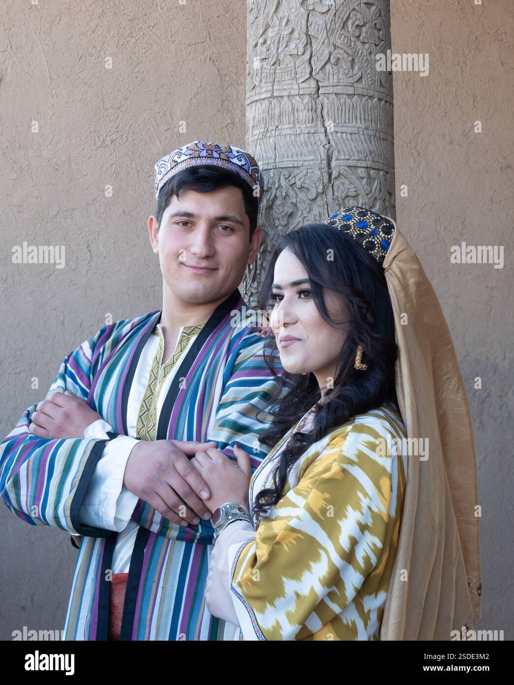 Das lächelnde junge usbekische Paar mit traditioneller Kleidung aus Ikat-Stoff posiert für ein Porträt eines anderen Fotografen. Stockfoto