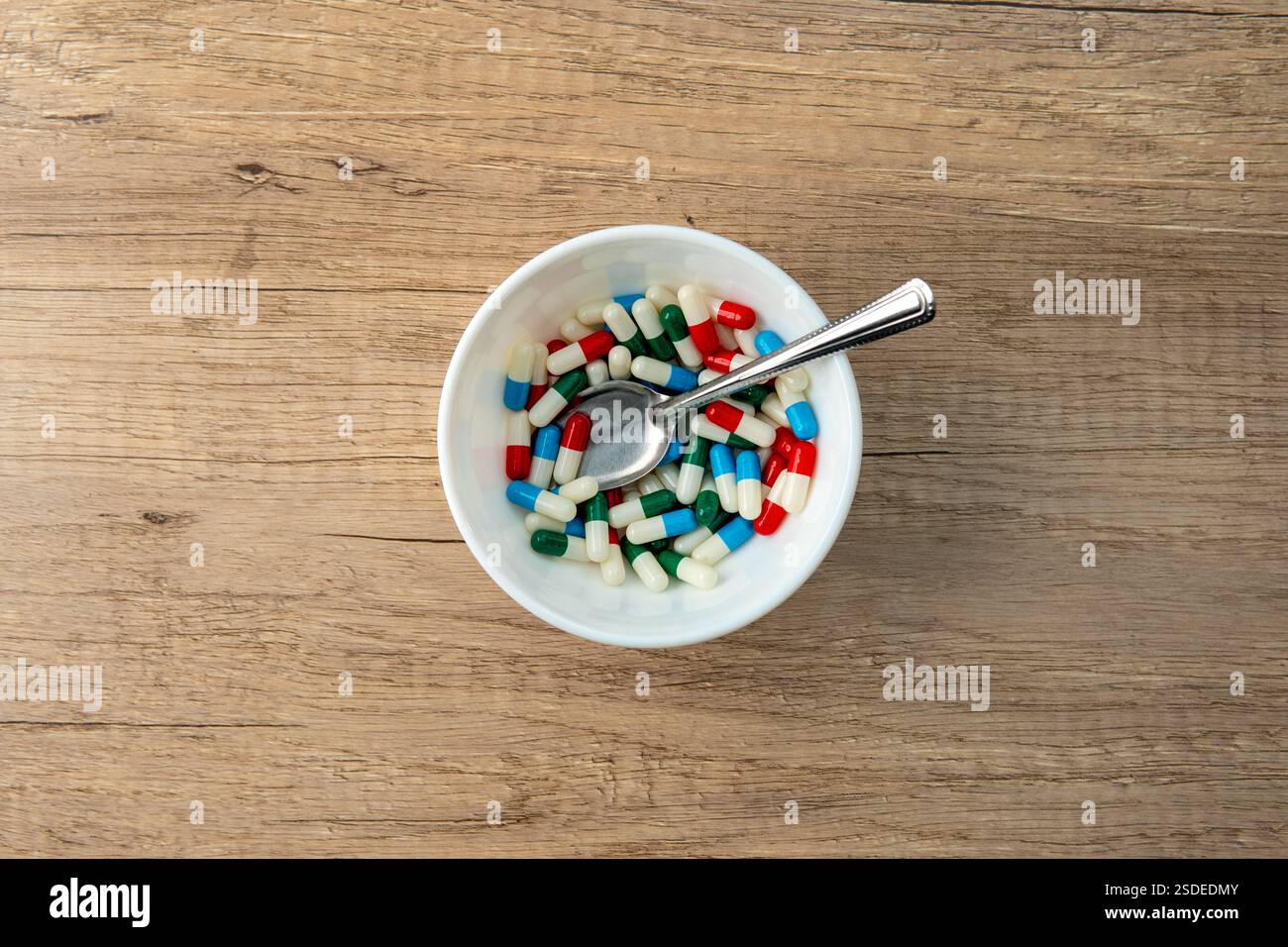 Eine weiße Schüssel gefüllt mit bunten Kapseln und einem Löffel. Medizin- und Gesundheitskonzept. Stockfoto
