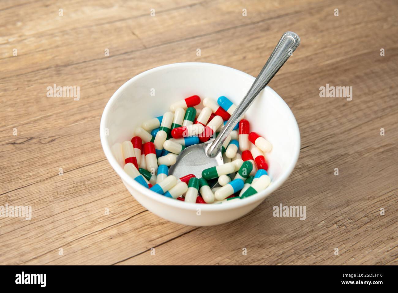 Eine weiße Schüssel gefüllt mit bunten Kapseln und einem Löffel. Medizin- und Gesundheitskonzept. Stockfoto