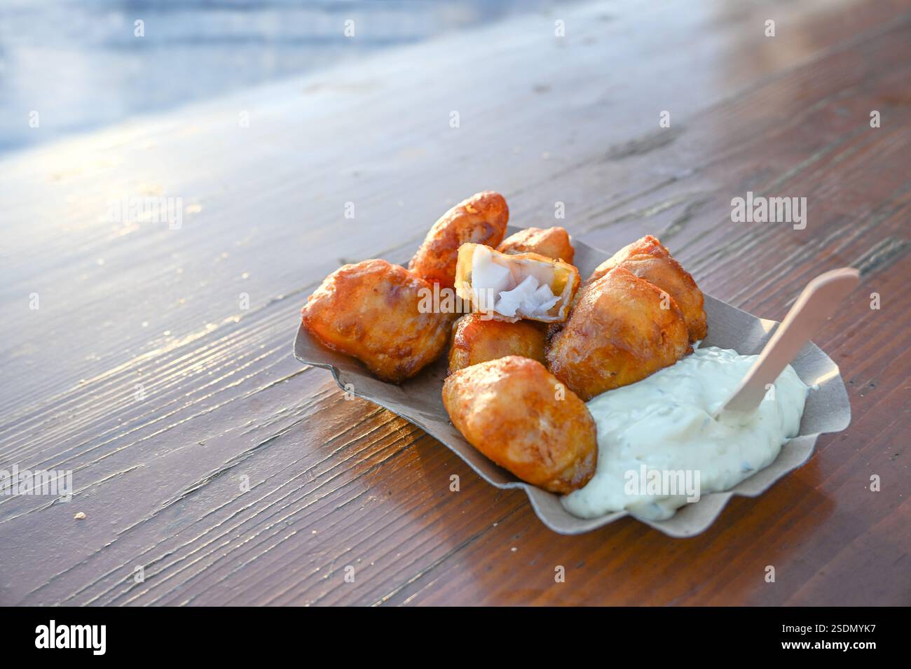 Frittierte Bierteig Kabeljaustücke mit Remoulade-Sauce auf einer Pappe auf einem Holztisch, Fischgericht zum Mitnehmen bei einem Meeresfrüchtegrill am Hafen, Stockfoto