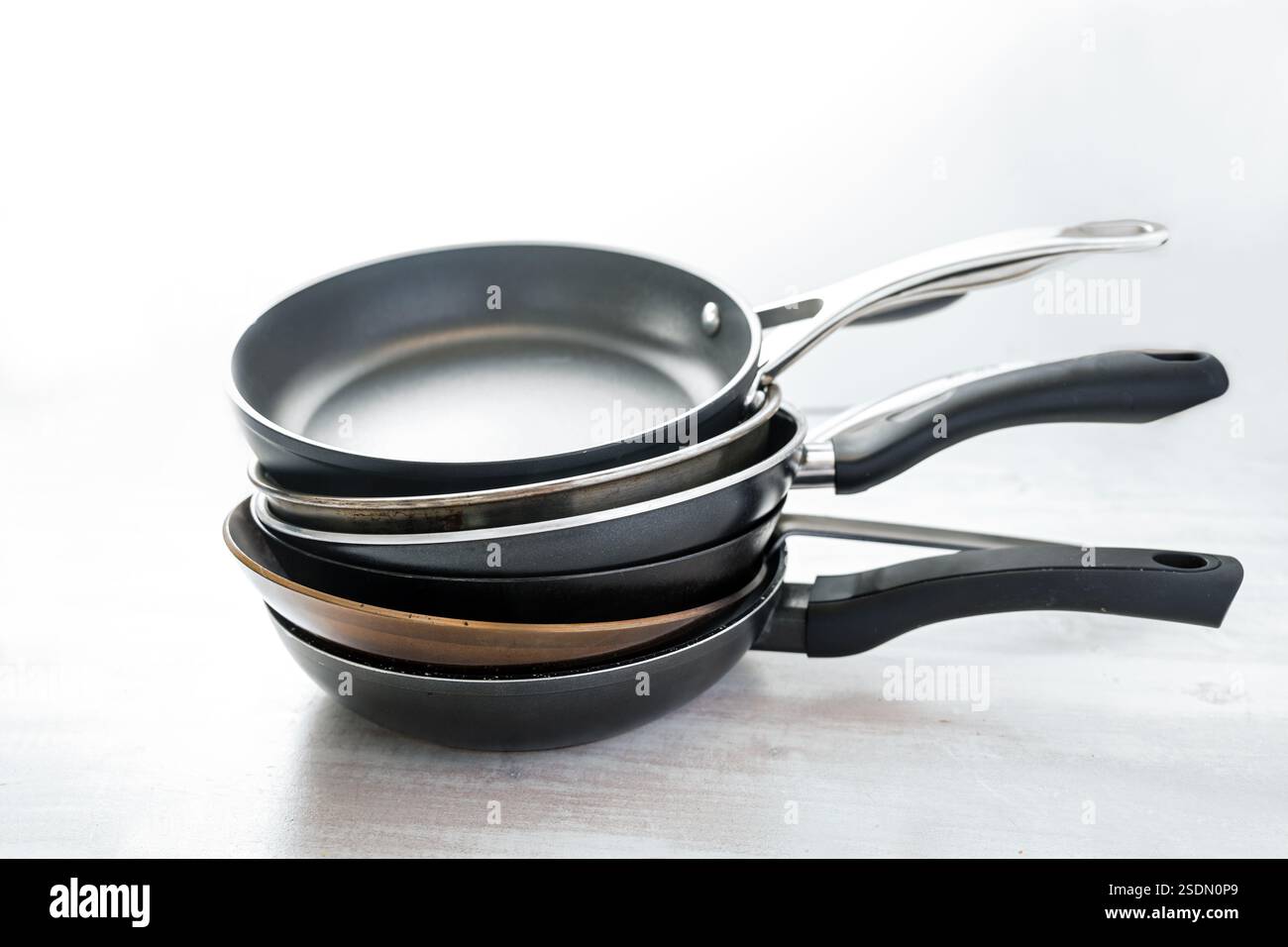 Stapel von verschiedenen Pfannen aus Gusseisen, Karbonstahl, Antihaftbeschichtung und Edelstahl, Wahl des richtigen Küchengeschirrs, hellgraue Rückseite Stockfoto