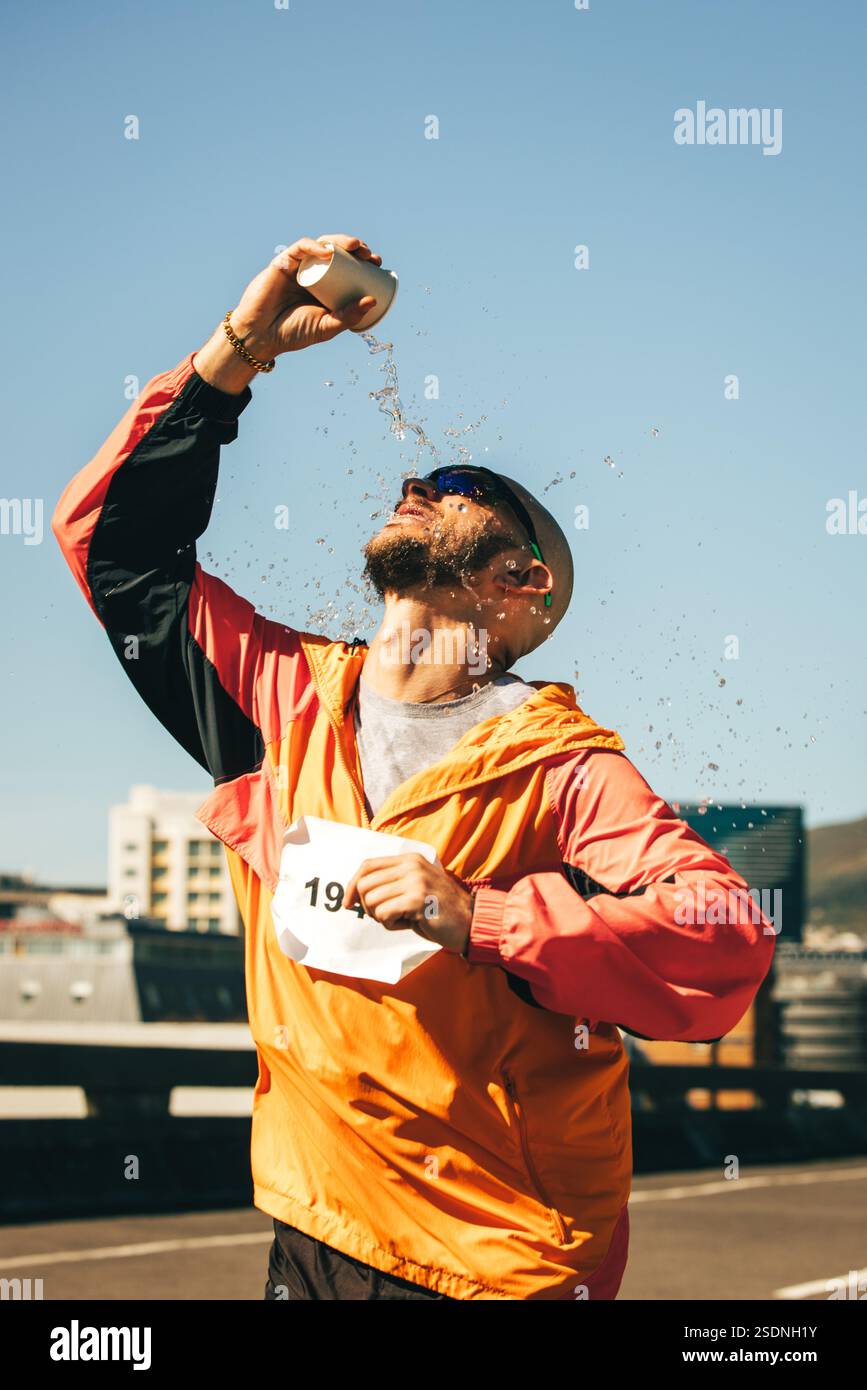 Ein Marathonläufer spritzt ihm während eines Rennens Wasser über das Gesicht. Dieser dynamische Moment spiegelt die Entschlossenheit und Belastbarkeit eines Athleten wider, der sich auf s konzentriert Stockfoto