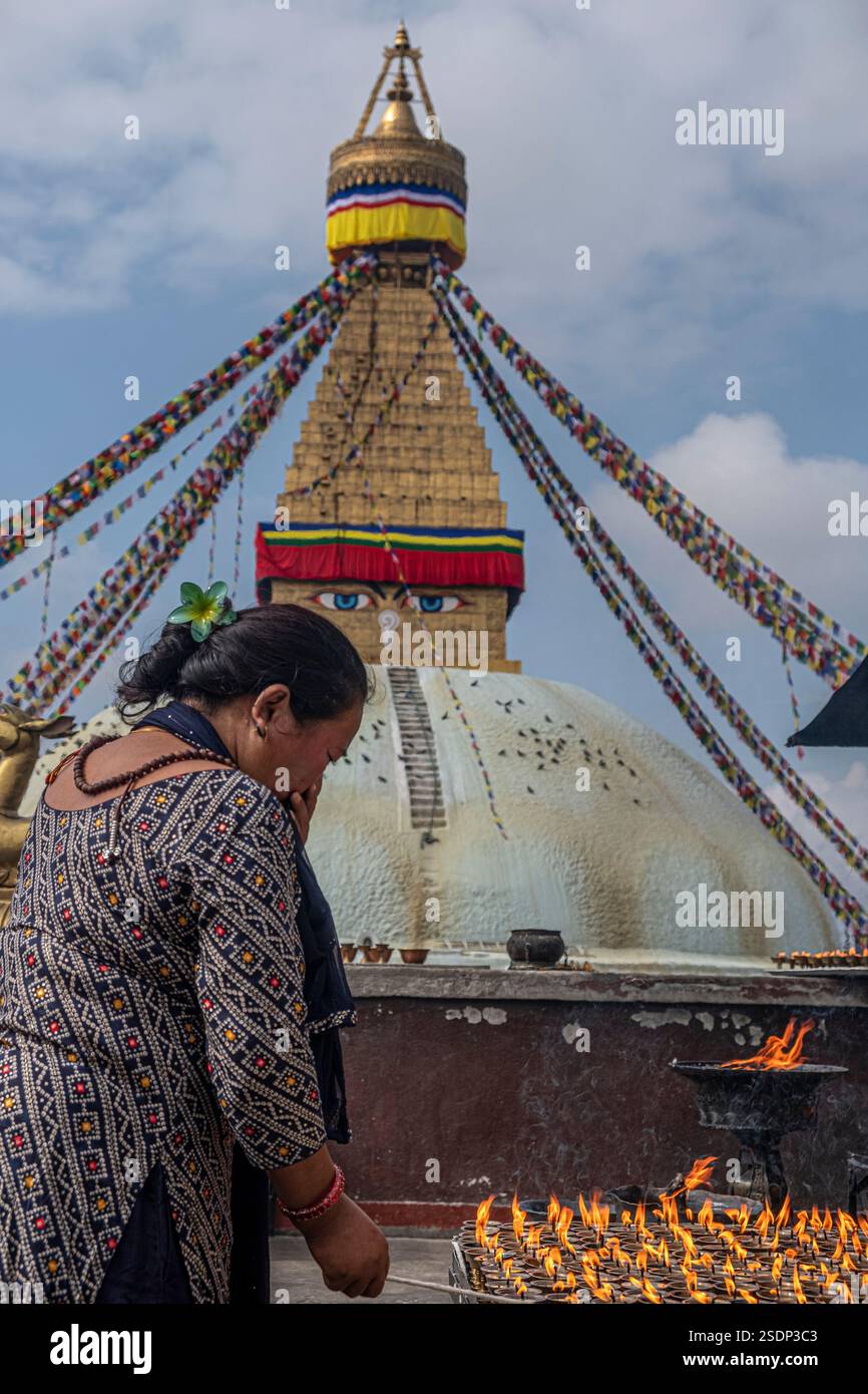 Eine Frau, die im Gebet vor der Boudhanath Stupa in Kathmandu, Nepal, steht, umgeben von brennenden Lampen und traditionellen tibetischen Dekorationen. Stockfoto
