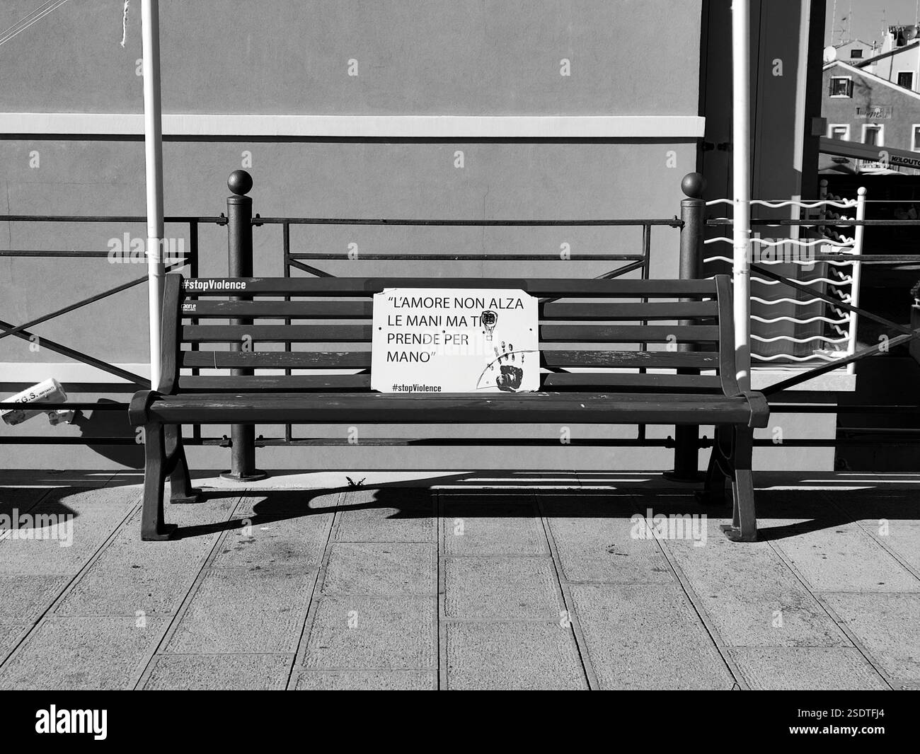 Ein Schwarzweißfoto einer leeren Parkbank mit einem Schild mit der Aufschrift „#stopViolence“ und „Love does not heves hands but take you by the Hand“ Stockfoto