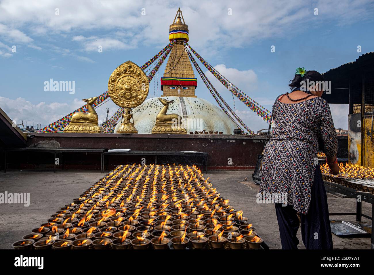 Eine Frau, die die Lampen vor der Boudhanath Stupa in Kathmandu, Nepal, vorbereitet. Sie ist von brennenden Lampen umgeben. Stockfoto