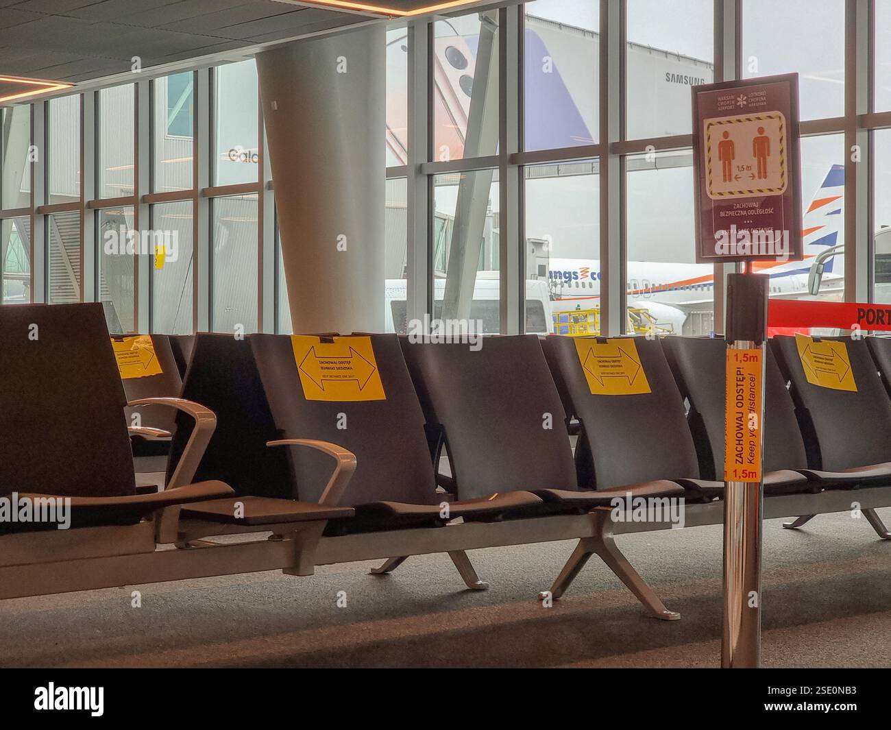 Leere Stühle im Flughafenterminal während der COVID-19-Pandemie mit Schildern, die darauf hinweisen, dass alternative Sitze nicht besetzt sein sollten, um Abstand zu halten - Smartphone-aufgenommenes Stockfoto