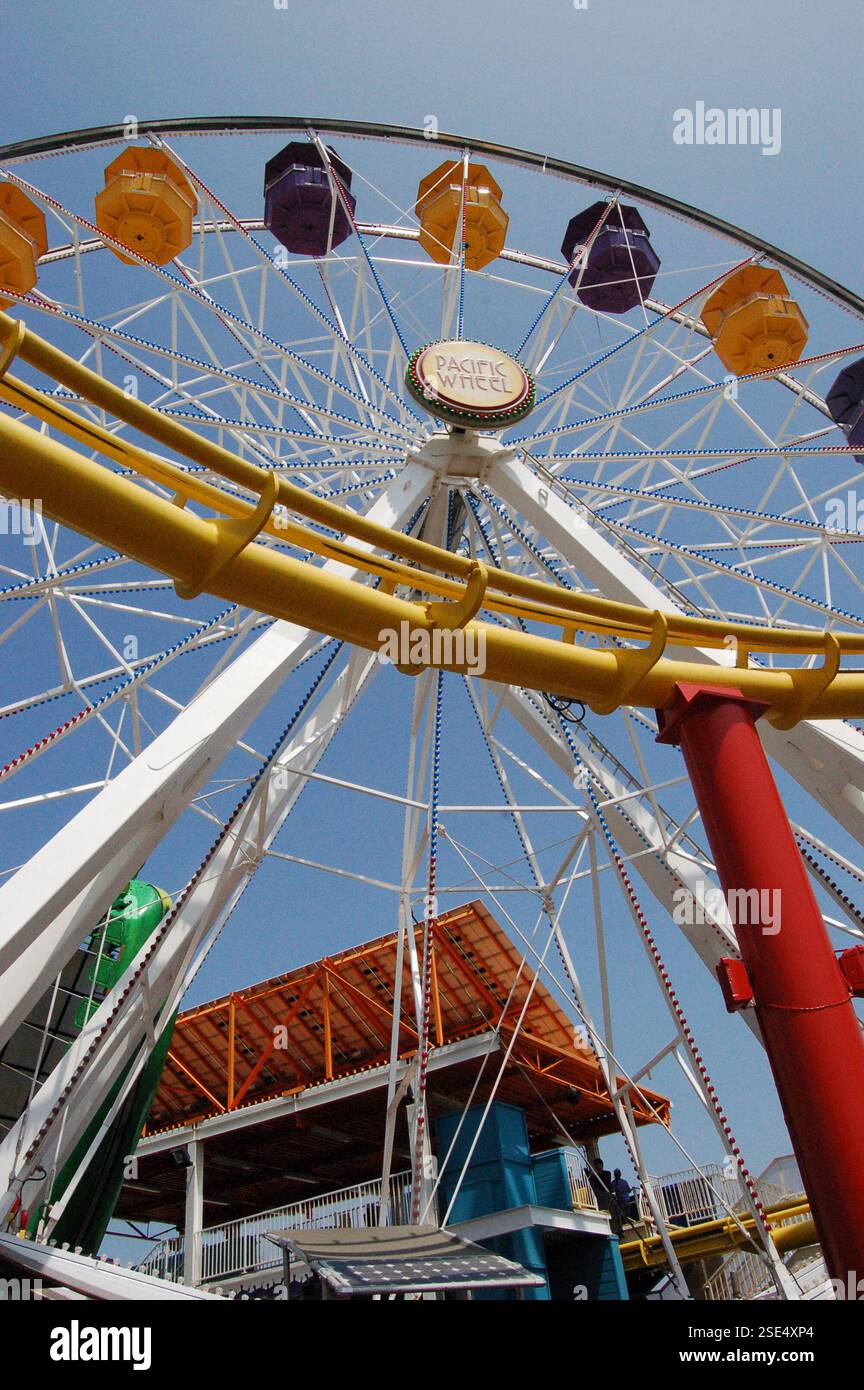 Sonniger Tag am Santa Monica Pier mit einer Kombination aus einem riesigen Riesenrad und einer Achterbahn über dem Ozean, die eine lebhafte Szene im Vergnügungspark schafft Stockfoto