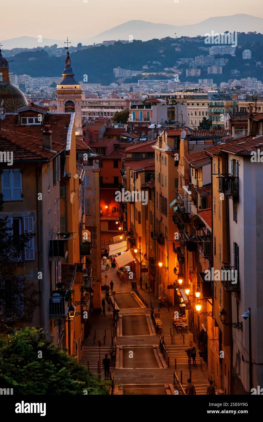 Ein bezaubernder abendlicher Blick auf die Altstadt von Nizza mit warmen Lichtern, die enge Gassen, historische Dächer und ferne Hügel unter dem sanften Glanz von t erhellen Stockfoto