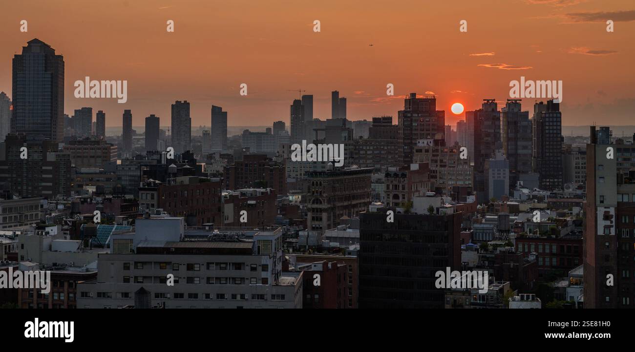 Während die Sonne untergeht, füllen die leuchtenden Orangetöne den Himmel über einer geschäftigen Skyline der Stadt, werfen Schatten auf die Wolkenkratzer darunter und schaffen eine atemberaubende Stockfoto