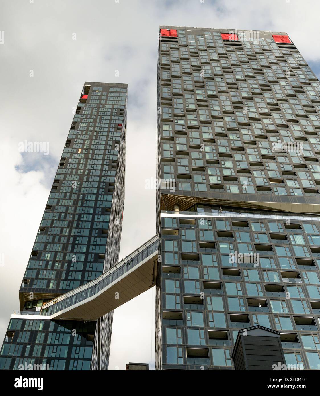 Zwei beeindruckende Hochhäuser stehen hoch, die durch eine elegante Himmelsbrücke verbunden sind. Die Gebäude sind mit reflektierendem Glas verkleidet und von einem dramatischen Clou umgeben Stockfoto