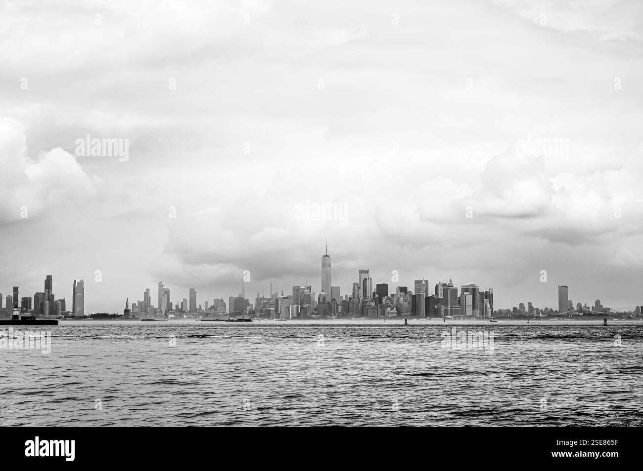 Vom Ufer aus ist eine entfernte Skyline der Stadt zu sehen, die von hohen Gebäuden unter einem stimmungsvollen Himmel dominiert wird. Wolken sammeln sich unheilvoll und verleihen dem Ur Tiefe Stockfoto