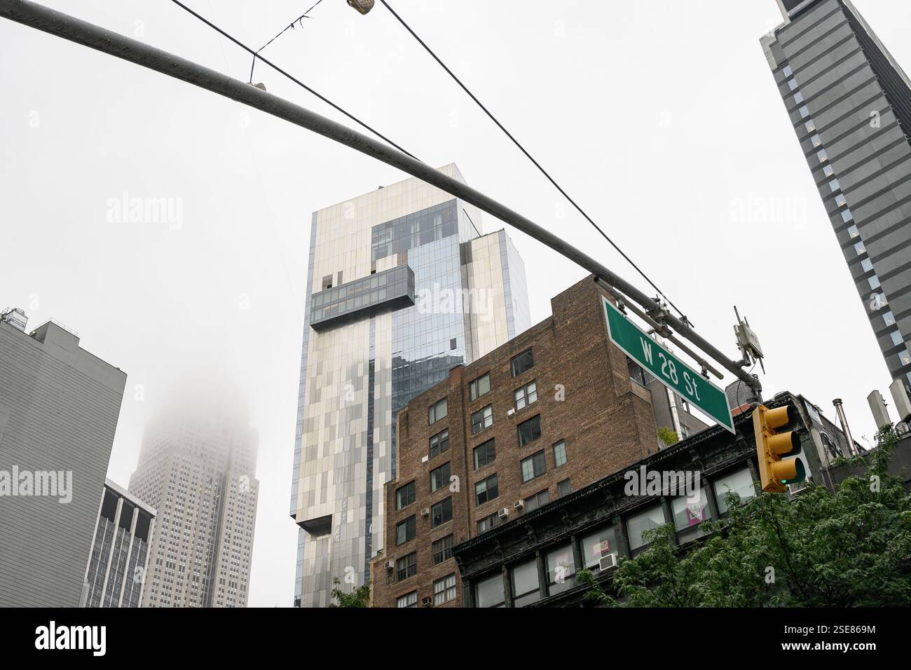 Ein nebeliger Tag in New York City zeigt einen Kontrast zwischen modernen Wolkenkratzern und älteren Gebäuden entlang der 28th Street, der urbanes Leben und Architektur zeigt Stockfoto