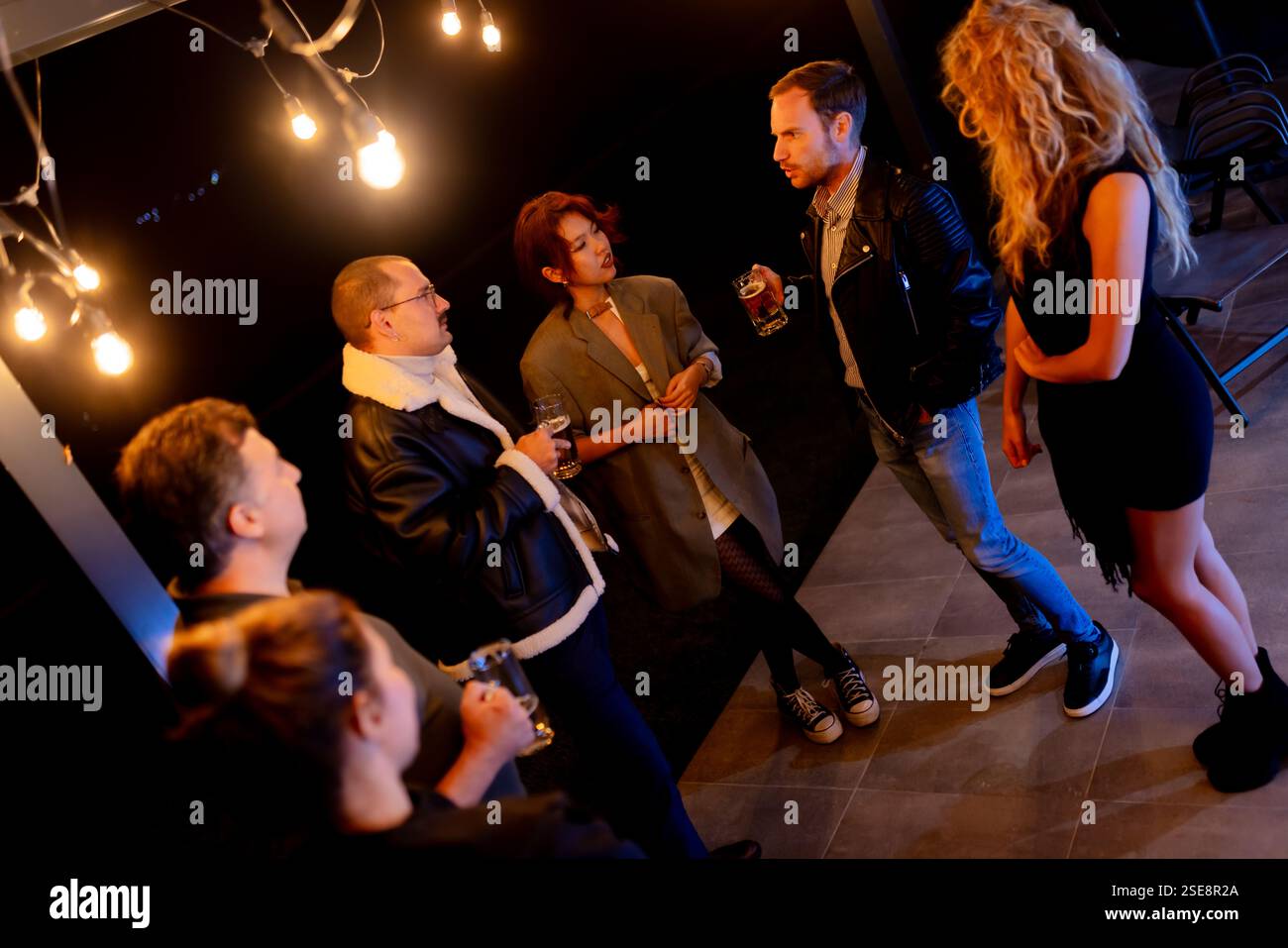 Enge Freunde, die sich in lebhaften Gesprächen unterhalten und Drinks während eines gemütlichen Abendessens, umgeben von warmer Beleuchtung, austauschen. Stockfoto