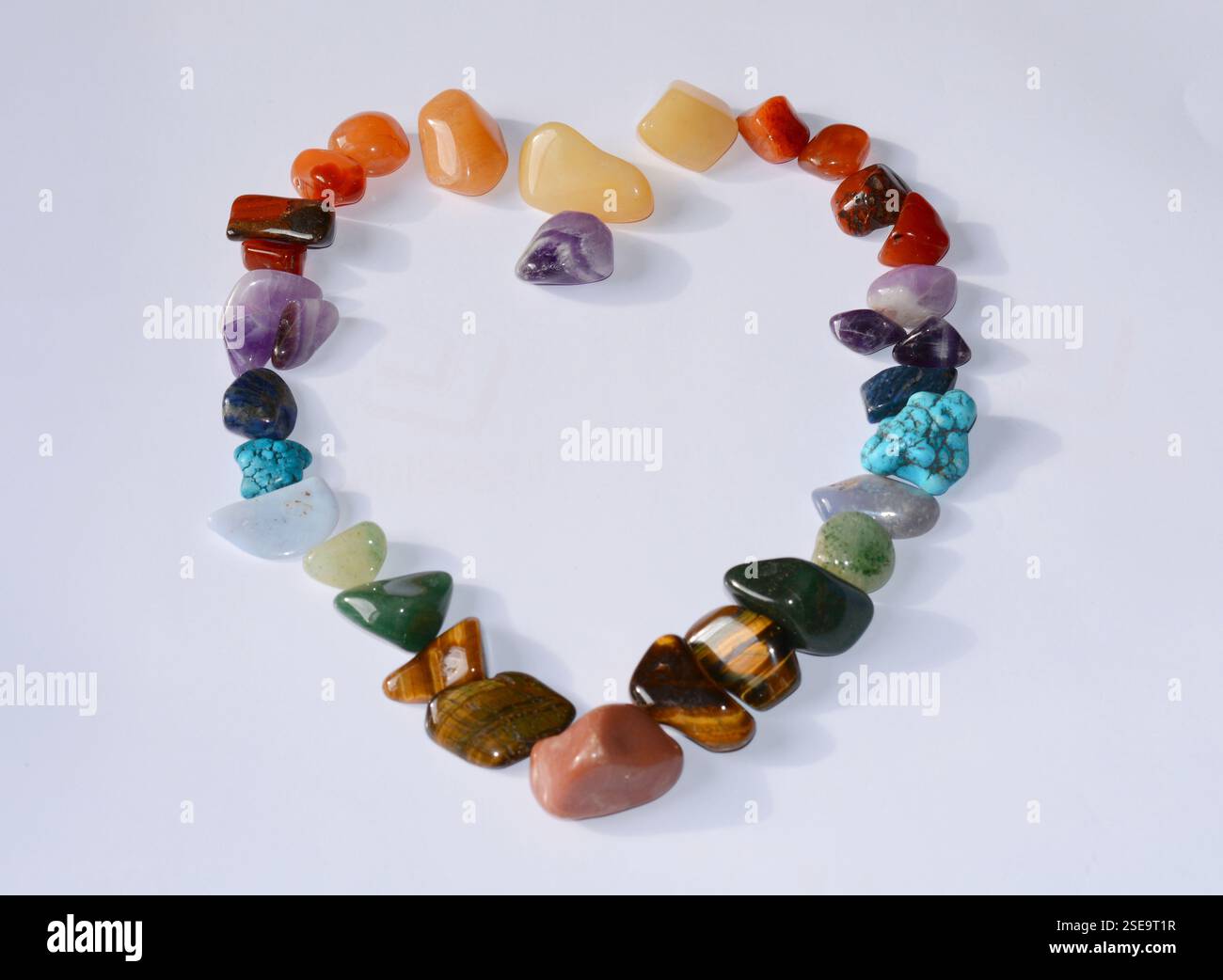Sammlung verschiedener roher Edelsteine wie Tigerauge, Amethyst, Zitrin, Quarz, jaspis, Malachit, in Herzform auf weißem Hintergrund platziert Stockfoto
