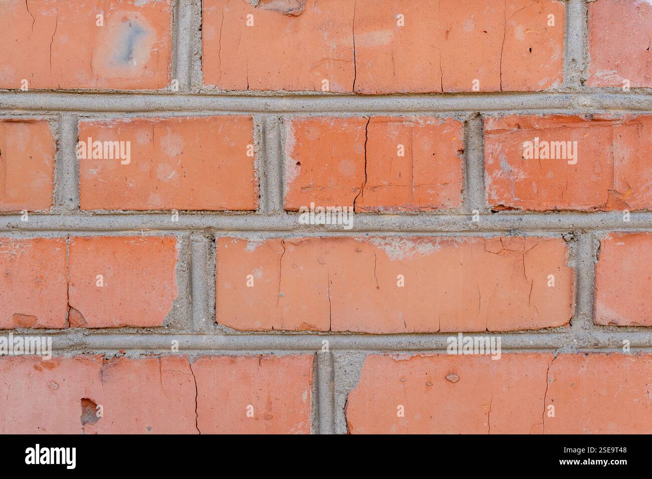 Eine alte rote Ziegelwand zeigt sichtbare Risse und verschlissenen Mörtel. Die Textur und Farbe zeigen die Geschichte der Wand und die Exposition gegenüber den Elementen über tim Stockfoto