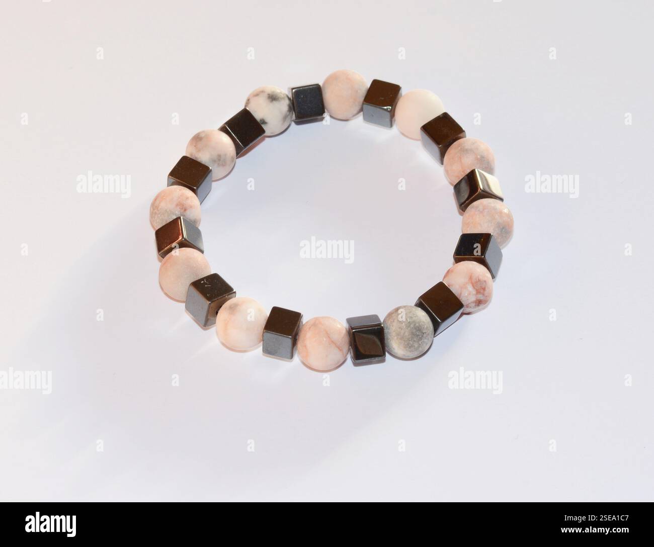 Eine lebendige Nahaufnahme eines bunten Edelsteinarmbands mit pfirsichfarbenen, braunen, weißen, schwarzen und grauen Quarzperlen vor weißem Hintergrund Stockfoto