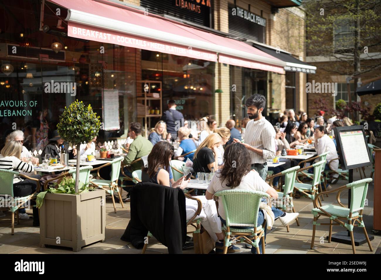 Speisen im Freien im libanesischen Restaurant Flavours of Lebanon im Londoner Sloane Square. Viele Gäste genießen den sonnigen Tag. Stockfoto