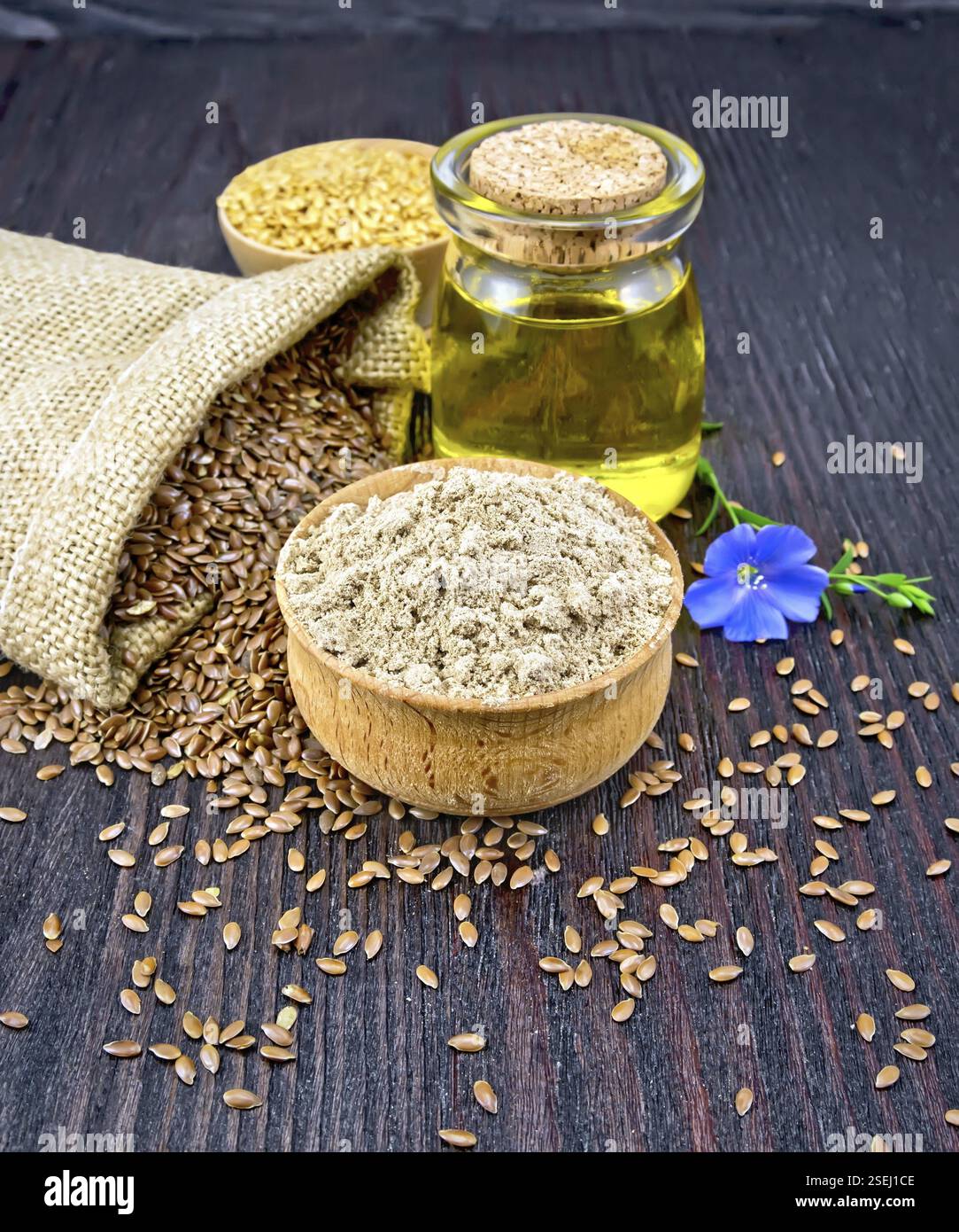 Flachs Mehl in eine Schüssel, Samen in einer Tasche, blau Bettwäsche Blume und Öl in einem Glas auf einem Holzbrett Hintergrund Stockfoto