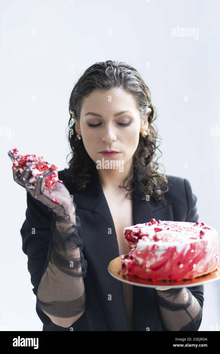Eine Frau, die einen teilweise gegessen Kuchen hält, besinnlicher Ausdruck Stockfoto