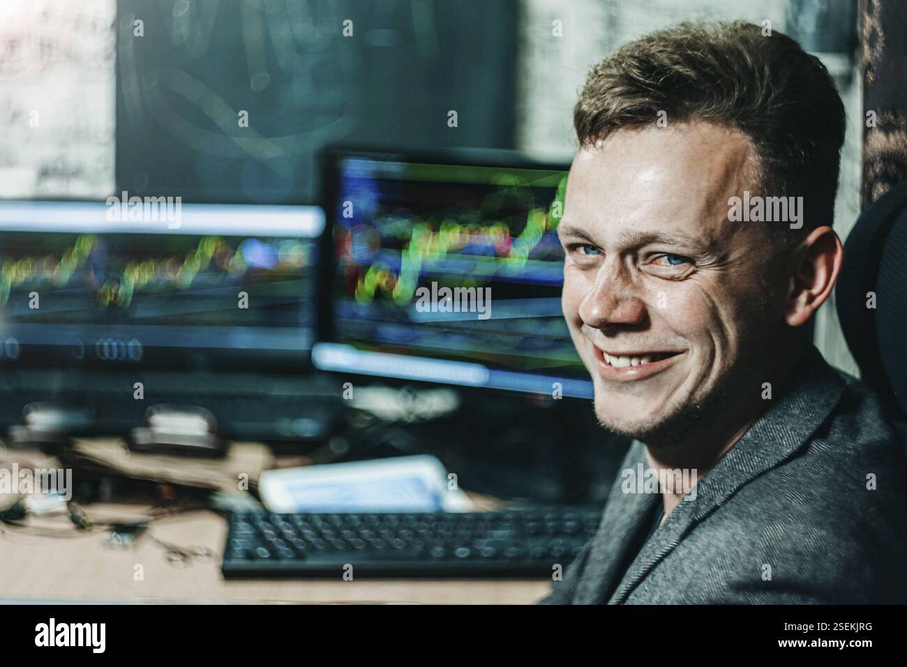 Ein Mann lächelt vor Computerbildschirmen und zeigt bunte Handelskarten Stockfoto