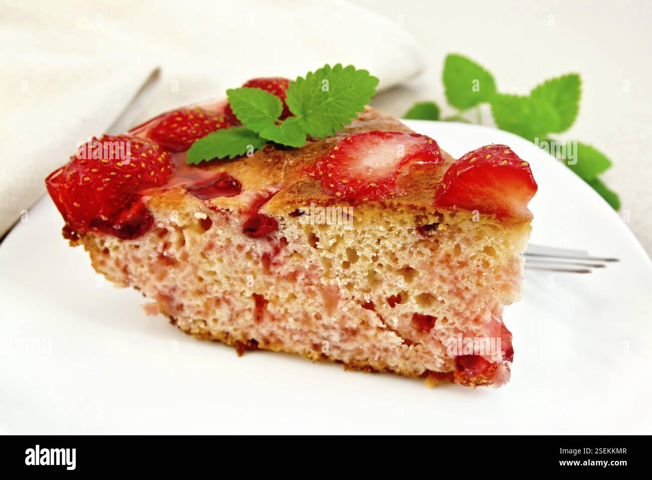 Stück süße Kuchen mit Erdbeeren, kissel, Gelee und Minze, eine Gabel in die weiße Platte auf dem Hintergrund Licht Holzbretter Stockfoto