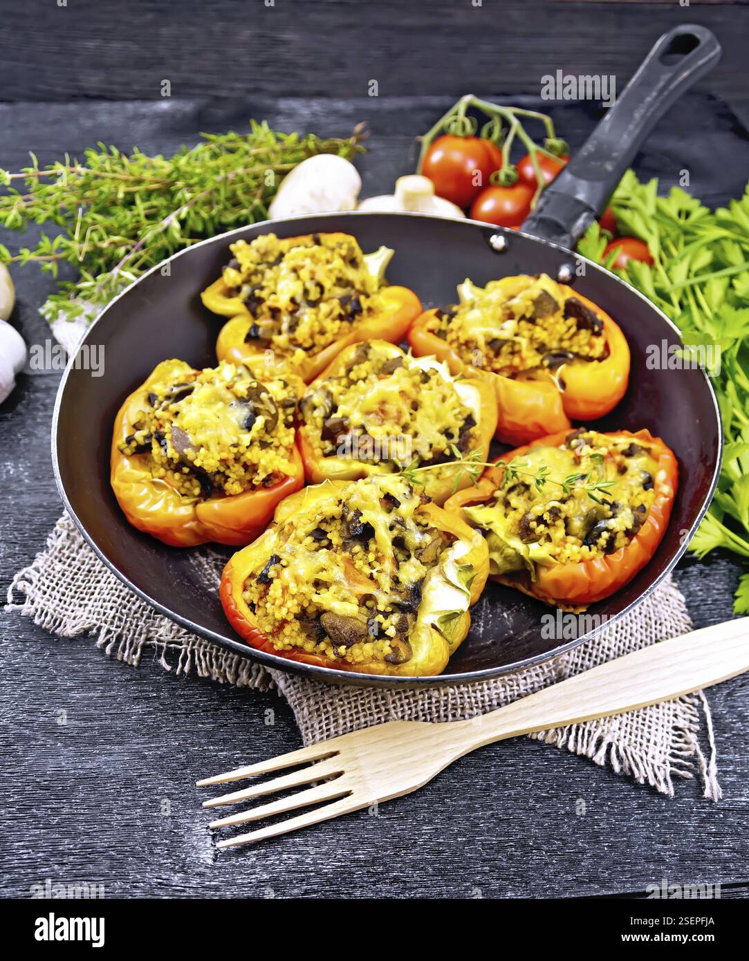 Paprika süss, gefüllt mit Pilzen, Tomaten, Couscous und Käse in eine alte Pfanne auf Sackleinen, eine Gabel, Petersilie und Thymian vor dem Hintergrund o Stockfoto