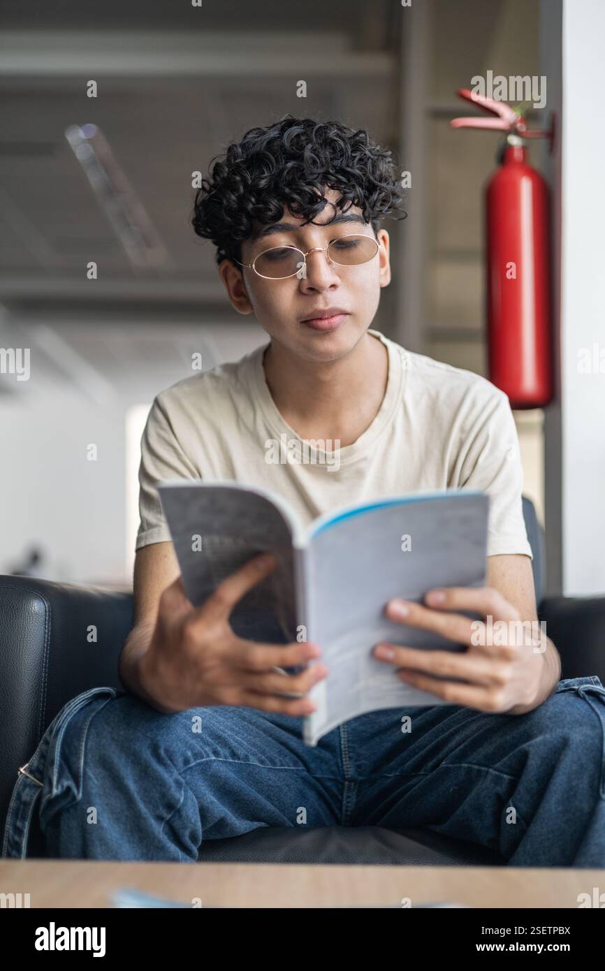 Eine Person, die eine Broschüre liest, während sie in einem komfortablen Wartezimmer wartet. Perfekt für Themen wie Entspannung, Warten und zwangloses Lesen. Stockfoto