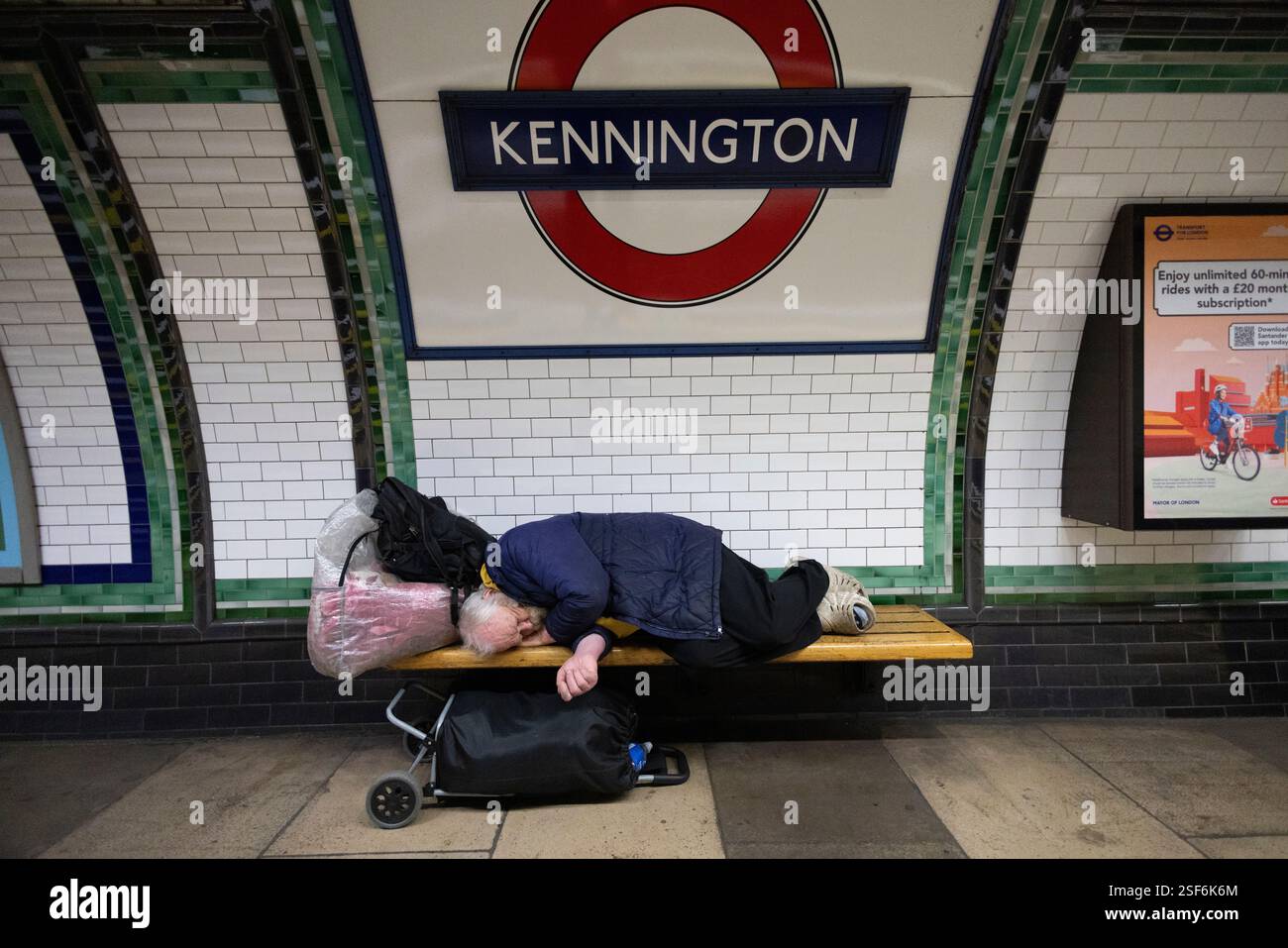 Ein Obdachloser schläft auf einer Londoner U-Bahn-Bank neben einem Bahnsteig an der Kennington Station, ohne die Passagiere oder den Lärm vorbeifahrender Züge zu vergessen. Stockfoto