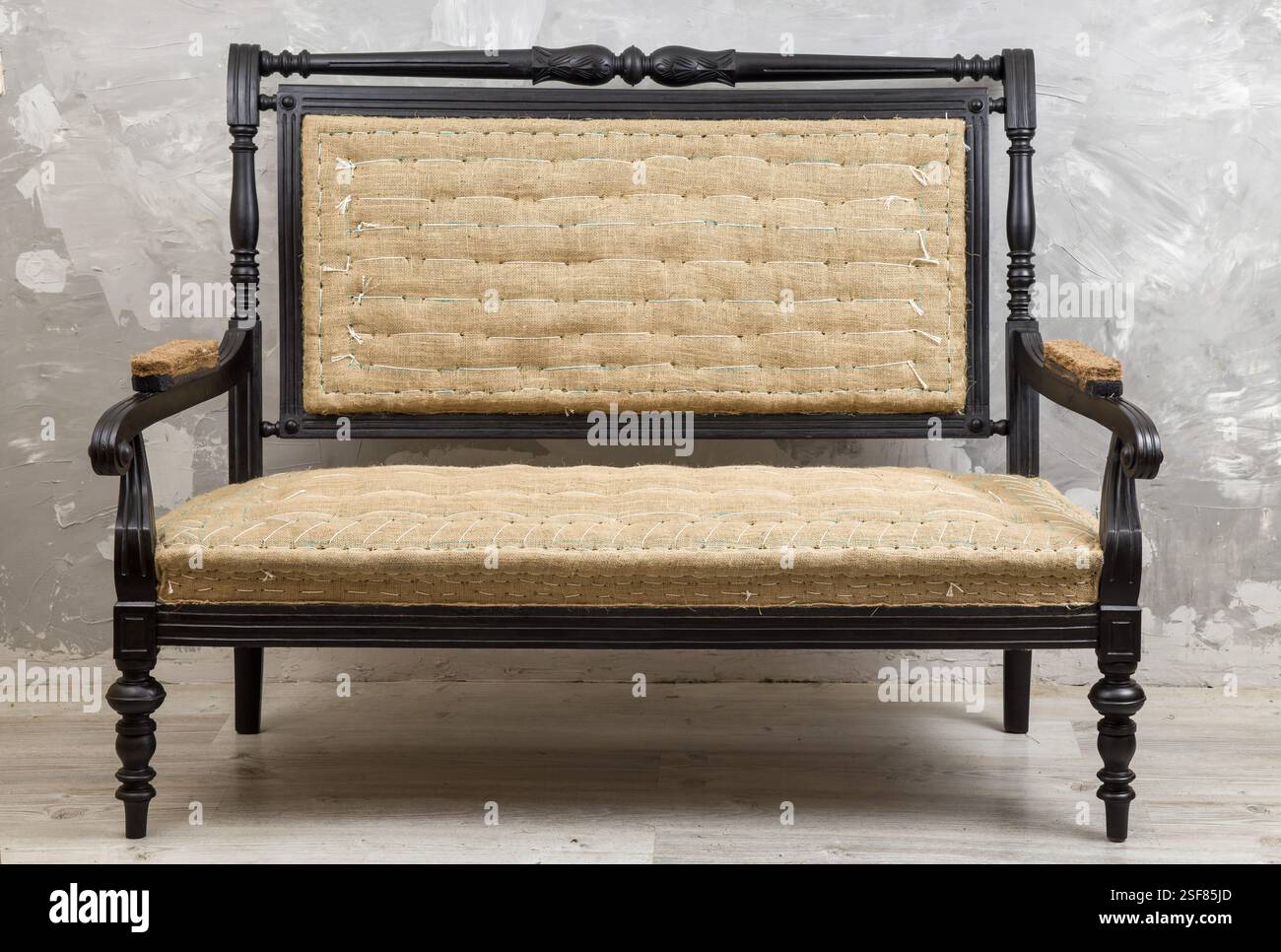 Antikes oder Vintage-Sofa mit dunklem Holzrahmen und hellen gewebten Polstern. Elegantes und klassisches Design vor strukturiertem Hintergrund. Perfekt für Pelze Stockfoto