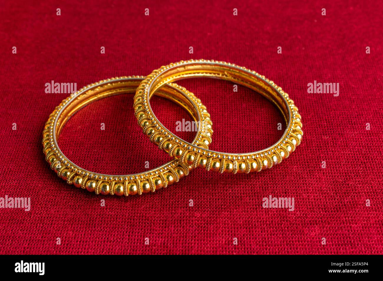Wunderschöne glänzende goldene Armreifen mit traditionellem indischem Design auf rotem Samthintergrund Stockfoto