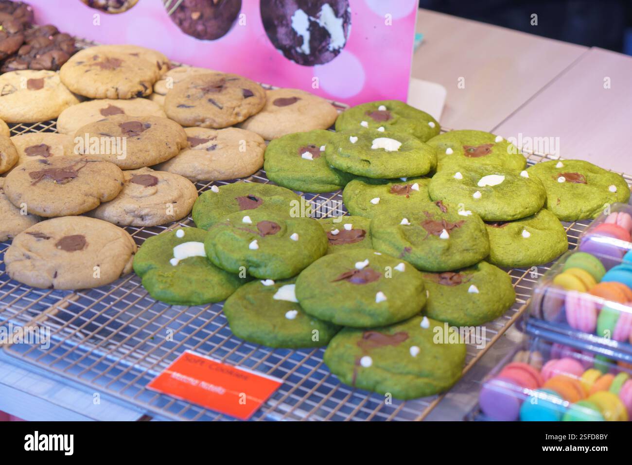 Nahaufnahme von frisch gebackenen Keksen an einem Konditorstand mit klassischen Schokoladenchips-Keksen und leuchtenden grünen Matcha-Keksen mit Schokoladenchu Stockfoto