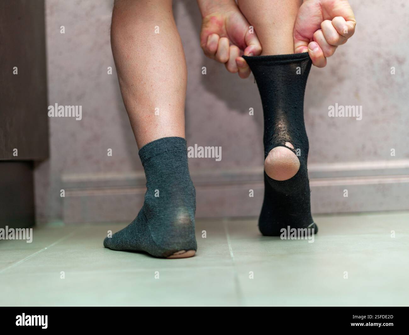 Ein Mann, der eine Socke mit einem Loch am Fuß steckt, in der Nähe Stockfoto