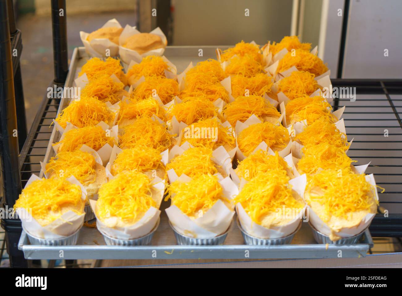 Nahaufnahme von weichen, flauschigen Cupcakes, gekrönt mit feinen Fäden aus goldenen Eiern (Foi Thong), ausgestellt an einem Street Food Stand. Dieses beliebte Thai Stockfoto