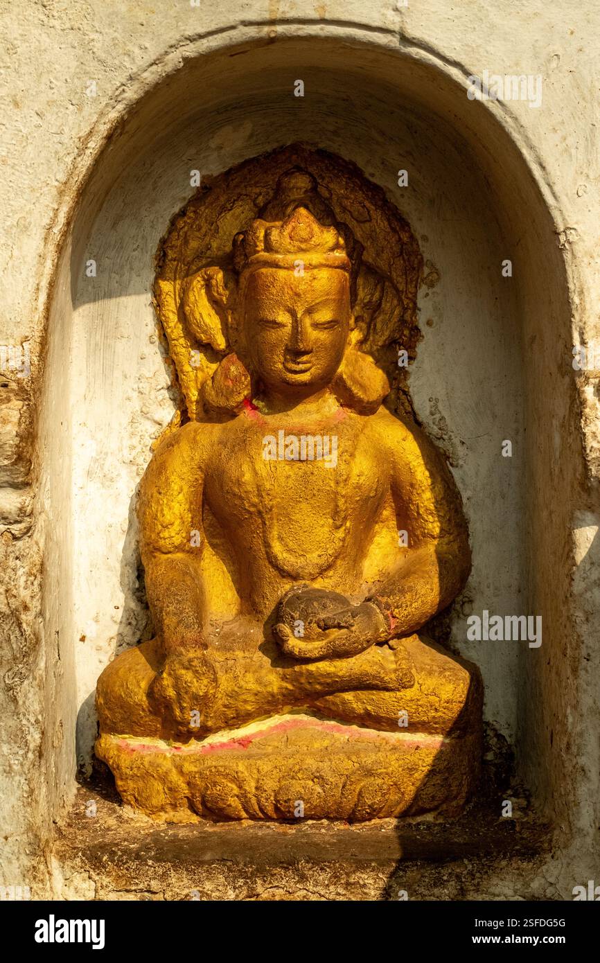 In Kathmandu ruht eine alte goldene Buddha-Statue in einer dekorativen bogenförmigen Nische auf einer Steinmauer, die Spiritualität und Ruhe ausstrahlt. Stockfoto