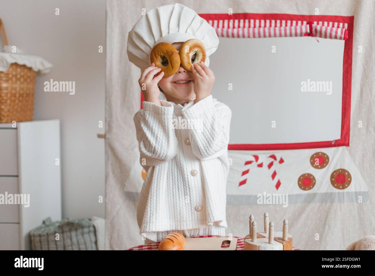 Ein lächelndes Mädchen, das sich als Konditorin ausgab, bedeckte ihre Augen mit frisch gebackenen Bagels Stockfoto