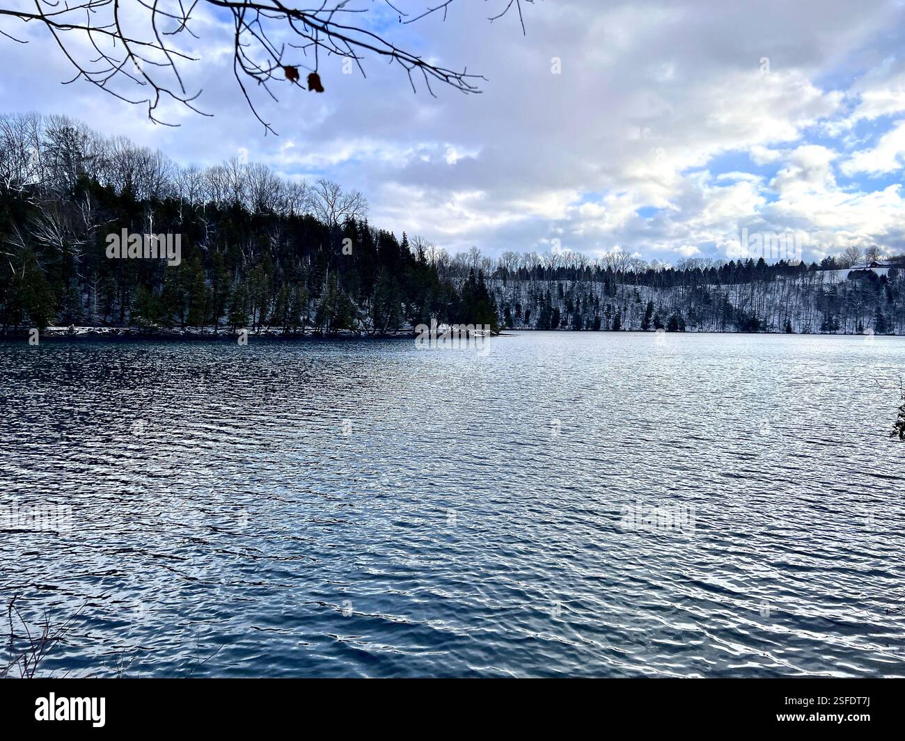 Wunderschöne Seeszene im Winter mit ruhigem Wasser, baumbestandenem und schneebedecktem Ufer. Sonniger Himmel mit Wolken. Keine Personen. Green Lakes, Syracuse NY. Kopierbereich. Stockfoto