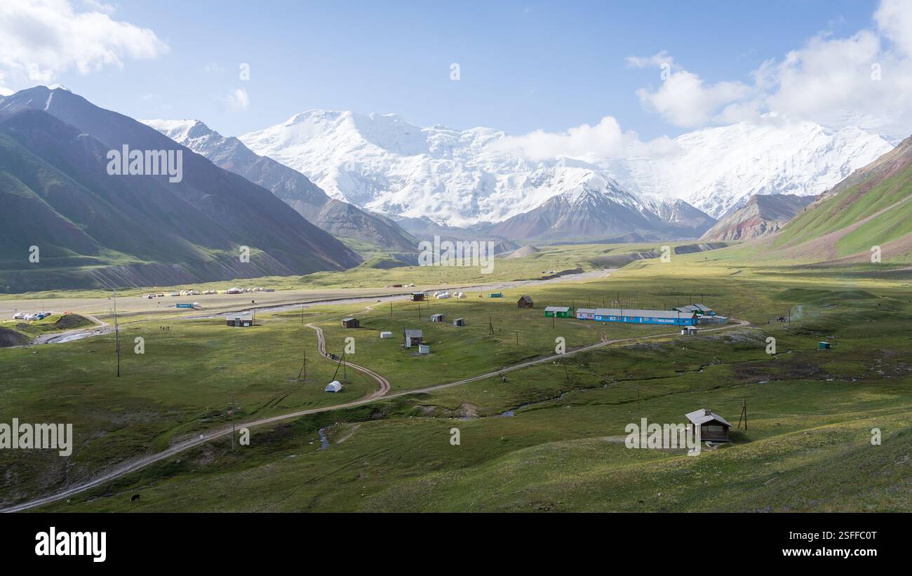 Blick auf das alpine Expeditionsbasecamp im grünen Tal unter den verschneiten Pamir Mountains, Kirgisistan Stockfoto