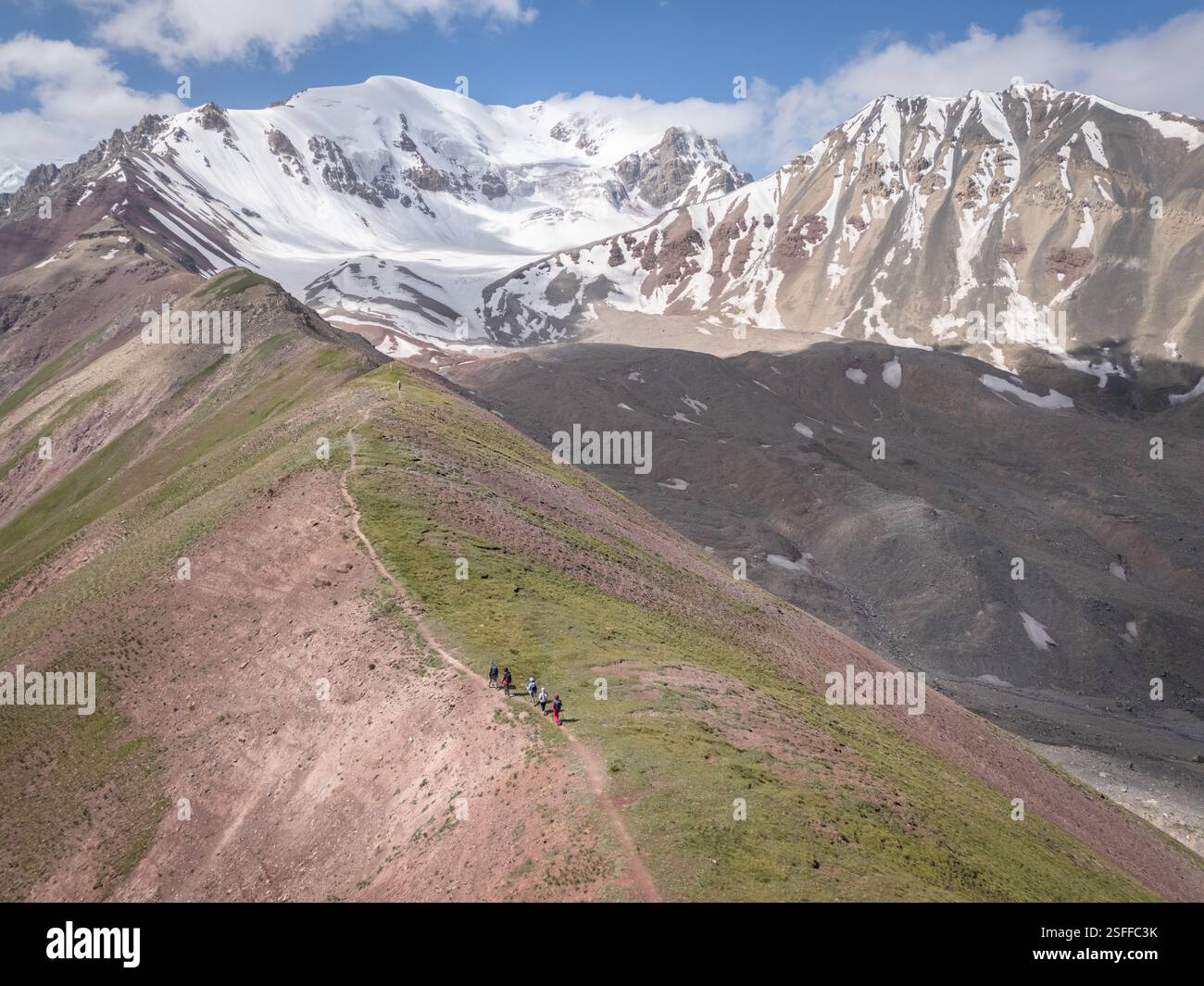 Blick aus der Vogelperspektive auf die alpine Landschaft mit Wanderern, die auf den schneebedeckten Pamir-Bergen in Kirgisistan wandern Stockfoto