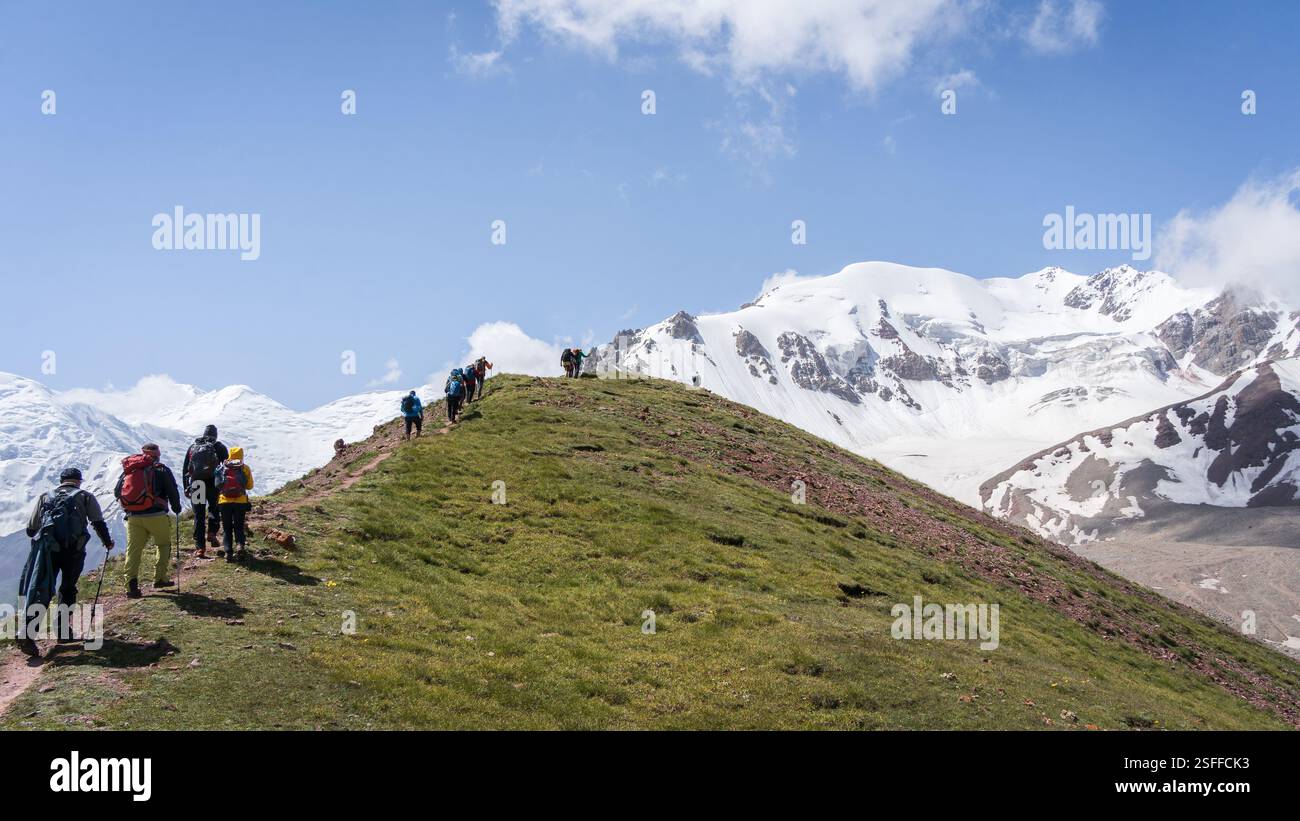 Gruppe von Wanderern, die den Bergkamm hinauf zu den schneebedeckten Gipfeln des Pamir-Gebirges in Kirgisistan aufsteigen Stockfoto