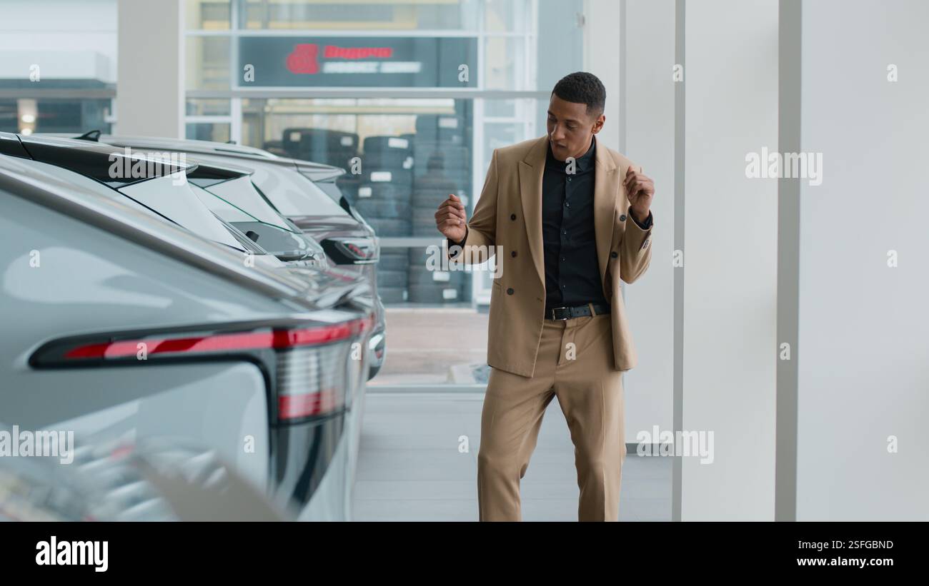 Glücklicher Autobesitzer Afroamerikaner feiert Tanzen aufgeregt Kauf eines neuen Autos im Showroom Autoverkauf lustiger Mann männlicher Käufer Kunde Geschäftsmann Stockfoto