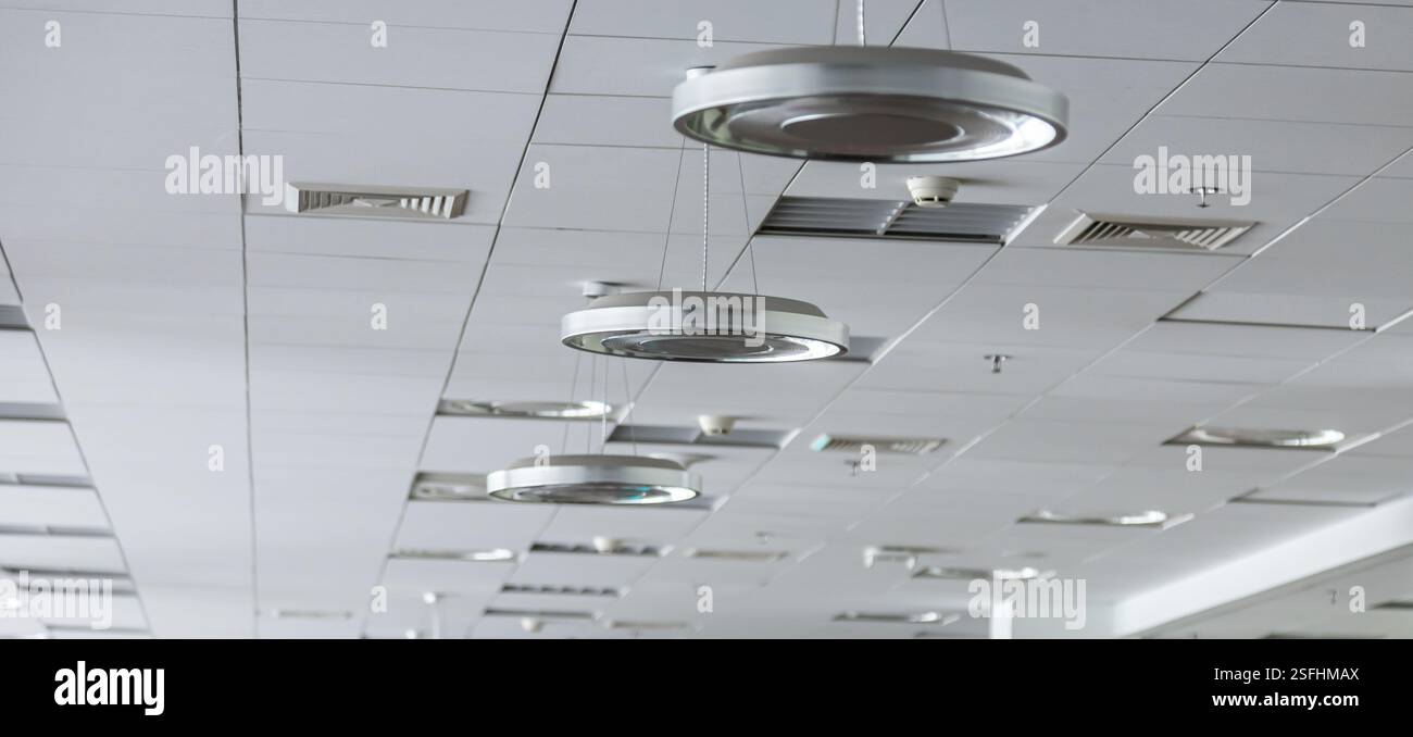 Das Deckendesign verfügt über schlanke Hängelampen und Lüftungsschlitze in einem modernen Büro, wodurch die Ästhetik und Funktionalität des Arbeitsplatzes verbessert wird. Stockfoto