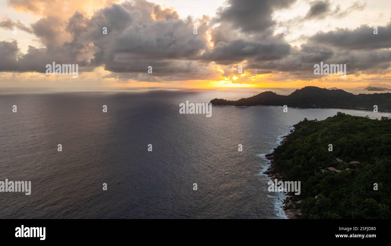 Sonnenuntergang über der Küste von Mahe mit dunklen Wolken und ruhigen Meeresgewässern. Seychellen, Mahe. Stockfoto